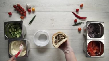Ekmeğin içinde shawarma yapan eldivenli profesyonel şefin elleri. Eldivenli şef shawarmaya sos koyar.
