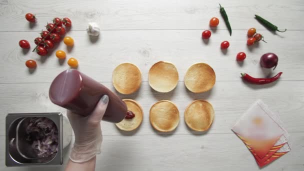 Vue de dessus du chef professionnel cuisine un délicieux hamburgers au restaurant de restauration rapide. Femme chef dans des gants met du ketchup sur trois pains rôtis pour hamburgers 