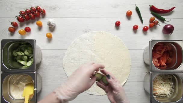 흰 장갑을 끼고 있는 요리사들의 손 이 위에 보이는 것을 보면, 피카 나라 바시에 있는 도너 케밥 샤와르마에 오이를 얹는다. 닭고기, 감자튀김, 치즈, 야채와 함께 샤와르마를 요리하는 모습 — 비디오