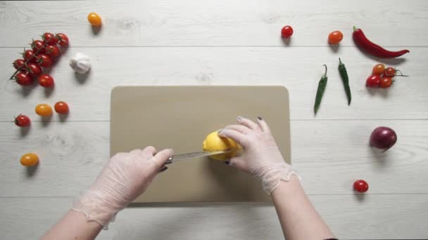 Chef händer i handskar skära en citron på hackbrädan. Handskivad citron på tavlan närbild. Saftig citron skuren i skivor. Den vassa kockkniven skär citrusfrukten. — Stockvideo