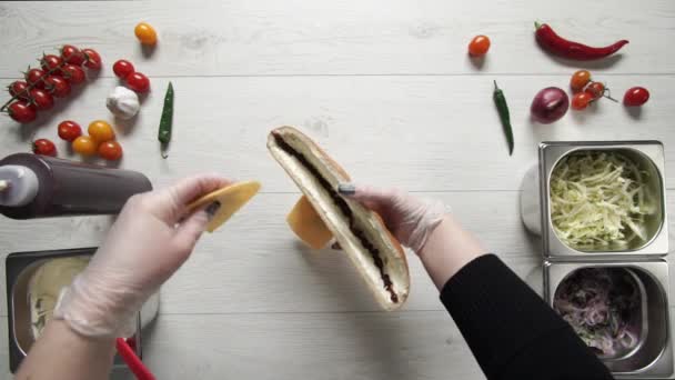 Vista dall'alto di mani di chef professionista in guanti che fanno shawarma su sandwich in pane. Lo chef in guanti mette il formaggio in sandwich — Video Stock