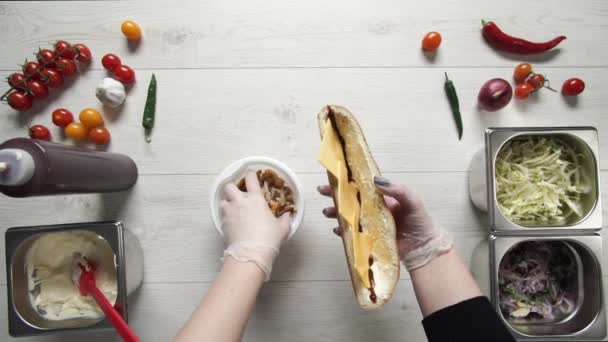 Draufsicht auf die Hände eines professionellen Kochs in Handschuhen, der Shawarma auf Sandwich im Brot zubereitet. Chef in Handschuhen legt Pommes und Hühnerfleisch ins Sandwich