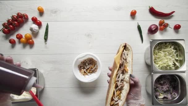 Vue du dessus des mains du chef professionnel dans les gants faisant shawarma sur le sandwich dans le pain. Chef en gants met de la sauce barbecue en sandwich 