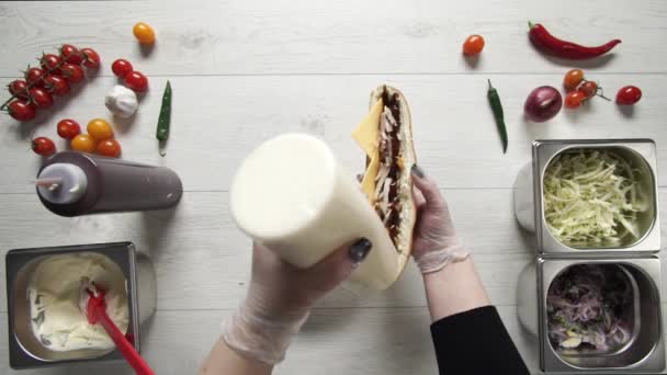 Bovenaanzicht van de handen van professionele chef-kok in handschoenen het maken van shawarma op sandwich in brood. Chef in handschoenen doet saus in sandwich — Stockvideo