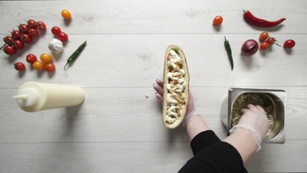 Вид зверху рук професійного шеф-кухаря в рукавичках, що роблять шаурму на бутерброд у хлібі. Шеф-кухар в рукавичках кладе капусту в бутерброд — стокове відео
