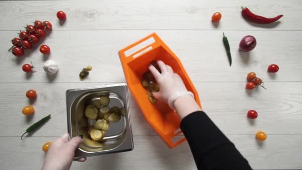 Le chef prend une tranche de cornichons dans un bol en plastique et les met dans un récipient en métal. 