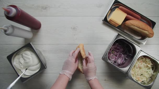 Bovenaanzicht van chef-kok handen in handschoenen kookt een hotdog, worst in het deeg. Chef opent broodjes en doet er hotdogs in — Stockvideo