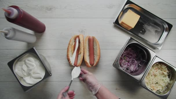 Pemandangan atas tangan koki dalam sarung tangan memasak hot dog, sosis dalam adonan. Koki menaruh saus di hot dog. — Stok Video