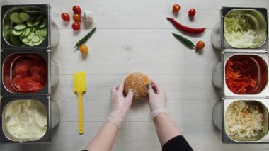 Profesyonel şef fast food restoranında lezzetli bir hamburger pişiriyor. Eldivenli kadın aşçı masadaki bir sakalı açıyor.