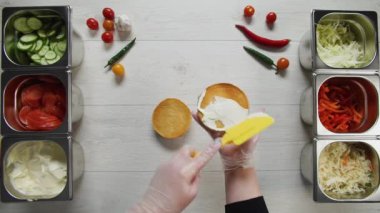 Profesyonel şef fast food restoranında lezzetli bir hamburger pişiriyor. Eldivenli kadın aşçı hamburgerler için şiş ekmek koyuyor.