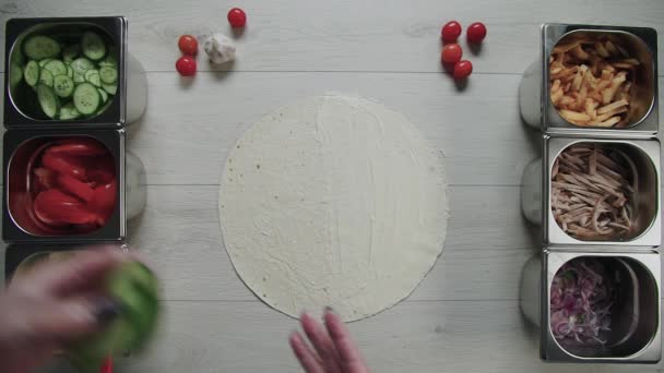 Vue du dessus des mains de chef en gants blancs met des concombres sur doner kebab shawarma en pita ou lavash. shawarma au poulet, frites, fromage et légumes — Video