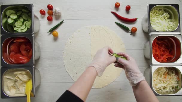 Von oben betrachtet legt Koch-Hände in weißen Handschuhen Gurken auf Dönerspieß Shawarma in Pita oder Lavasch. Shawarma mit Hühnerschnitzel, Paprika, Käse und Gemüse — Stockvideo