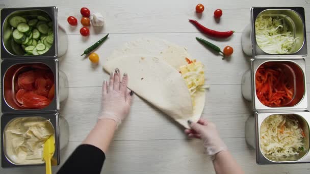 Вид зверху на руки шеф-кухаря в білих рукавичках обгортає донорську шаурму шашлику в піті або лаваші. Шаурма з курячою котлетою, паперами, сиром та овочами — стокове відео