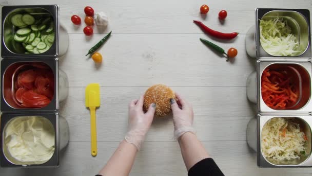 Top pohled na profesionální kuchař vaří lahodný burger v fast food restauraci. Ženské kuchařky v rukavicích otevírají jednu bradku pro hamburger na stole — Stock video