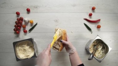 Profesyonel şef fast food restoranında lezzetli bir sandviç pişiriyor. Eldivenli kadın aşçı sandviçe sos koyar.