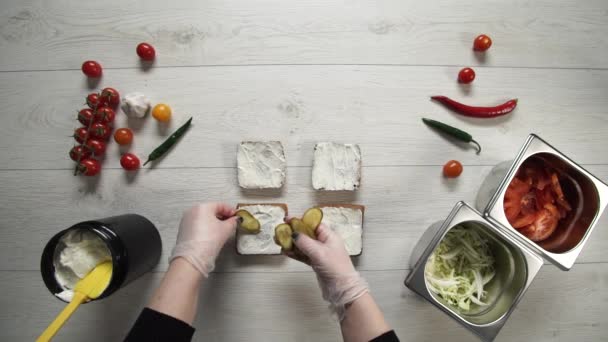 Vue de dessus du chef professionnel cuisine un délicieux hamburgers au restaurant de restauration rapide. Femme chef dans des gants met des cornichons sur les hamburgers — Video