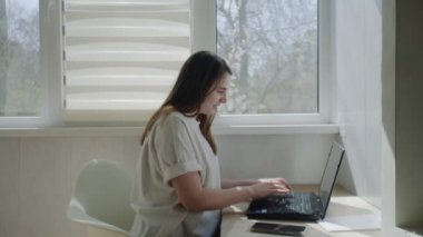 Dizüstü bilgisayar kullanan ve evde telefonla konuşan serbest çalışan kadınların yan görüntüsü.