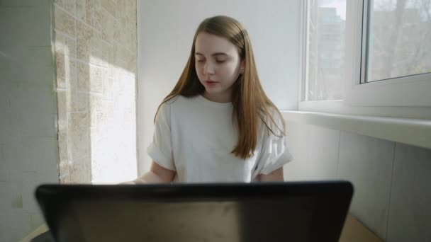 Mujer joven mirando en la pantalla del teléfono inteligente y trabajando en el ordenador portátil desde casa debido a coronavirus auto aislamiento. Auténtico lugar de trabajo en casa. Disparo de mano con cardán. Brote de Coronavirus 2020 . — Vídeo de stock