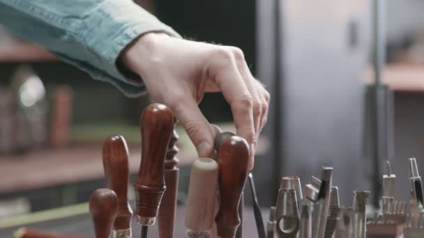 Der Gerber greift zum Punsch, um mit Leder zu arbeiten. Viele verschiedene Werkzeuge für die Handarbeit. Metallwerkzeuge — Stockvideo