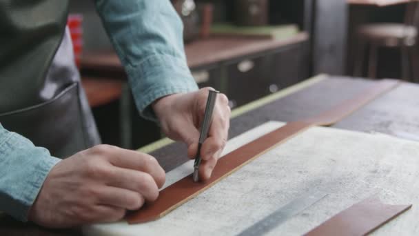 Tanner makes holes in belt. Working process of the leather belt in the leather workshop. Man holding crafting tool and working. Tanner in old tannery. — Stock Video