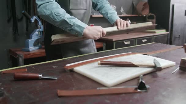 Proces pracy pasa skórzanego w warsztacie skórzanym. Człowiek trzyma narzędzie rzemiosła i pracuje. Tanner w starej garbarni. — Wideo stockowe