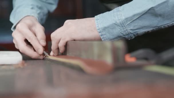 Un artesano de cuero está cortando los bordes de un cinturón. El maestro está utilizando una herramienta de biselado de borde . — Vídeo de stock