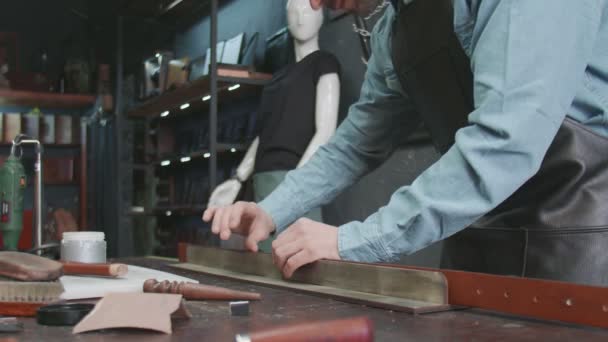 Profi tanner ember tesz paszta szélén egy öv a műhelyben. A bőröv munkafolyamata a bőrműhelyben. — Stock videók