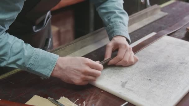 Großaufnahme eines Mannes mit Schürze, der in der Lederwerkstatt einen neuen braunen Ledergürtel herstellt. Arbeitsprozess des Ledergürtels in der Lederwerkstatt. — Stockvideo