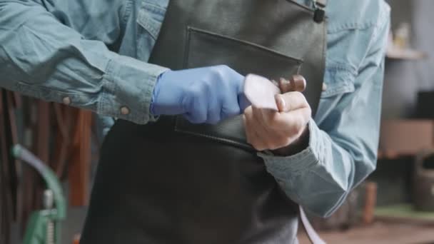 Un artigiano della pelle strofina i bordi di una cintura. Il padrone sta usando lo strumento sfregamenti . — Video Stock
