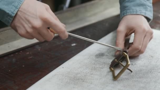 Primer plano de hombre curtidor con delantal utiliza un destornillador para la artesanía de un cinturón de cuero marrón en el taller de cuero. Proceso de trabajo del cinturón de cuero en el taller de cuero . — Vídeos de Stock
