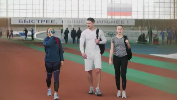 Tres amigos vienen a la arena deportiva y saludan con las manos a sus amigos — Vídeo de stock