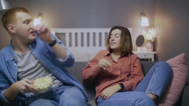 Genç mutlu adam ve kız TV 'de ilginç bir film izliyorlar. Oturma odasındaki kanepede patlamış mısırla birlikte. Karantina, salgın hastalık, virüs. Evde kal. — Stok video