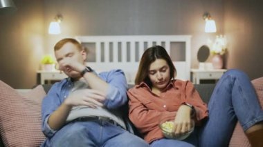 Sıkıcı genç adam ve kadın kanepede oturur, patlamış mısır yer ve televizyon izlerler.