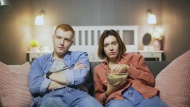 Sıkıcı genç adam ve kadın kanepede oturur, patlamış mısır yer ve televizyon izlerler.