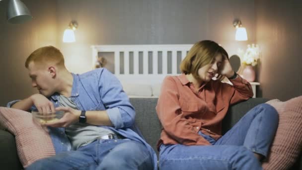 Ссорившиеся мужчина и женщина сидят на диване и едят попкорн — стоковое видео
