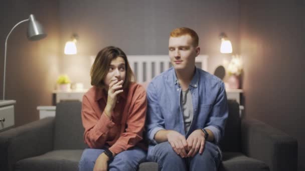 Happy young man and woman sitting on the sofa looking at the camera and flirting — Stock Video