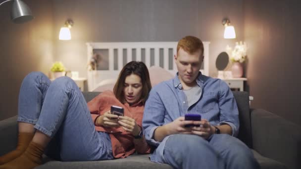 Молодой человек и женщина сидят на диване и используют смартфон — стоковое видео