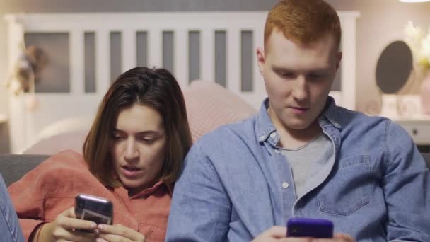 Young man and woman sits on couch and uses smartphone — Stock Video