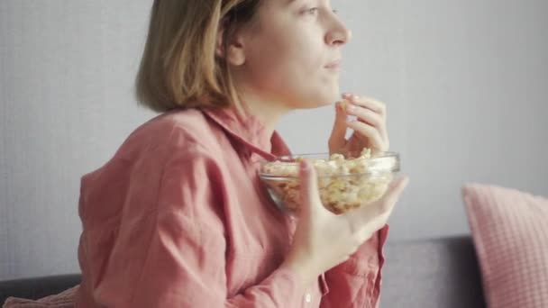 Молодая восторженная женщина сидит на диване, ест попкорн и смотрит телевизор — стоковое видео