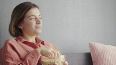 Genç, mutlu bir kadın kanepede oturuyor ve televizyonda komedi filmi izliyor.