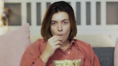 Genç bir kadın kanepede oturuyor, patlamış mısır yiyor, televizyon izliyor ve sızıyor.