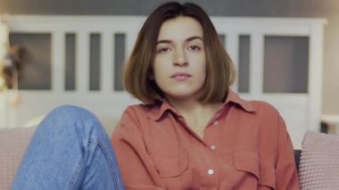 Genç bir kadın kanepede oturur ve televizyon izler. Kameraya bak.