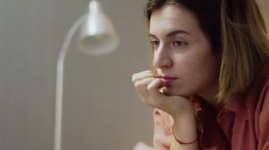 Genç, hayal kırıklığına uğramış, elinde bir fincan kahveyle kanepede oturup televizyon izleyen bir kadın.