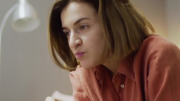 Young woman sitting on the sofa, eating popcorn and watching TV — Stock Video