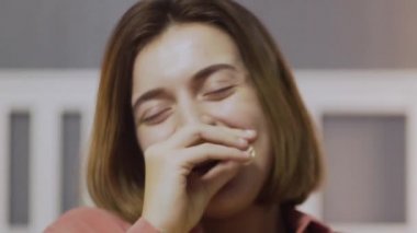 Kanepede oturan, patlamış mısır yiyen, komedi filmi seyreden ve gülen mutlu genç bir kadın.