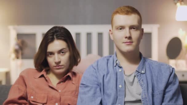 Happy young man puts hand on womans shoulder while sitting on the sofa and watching TV — Stock Video