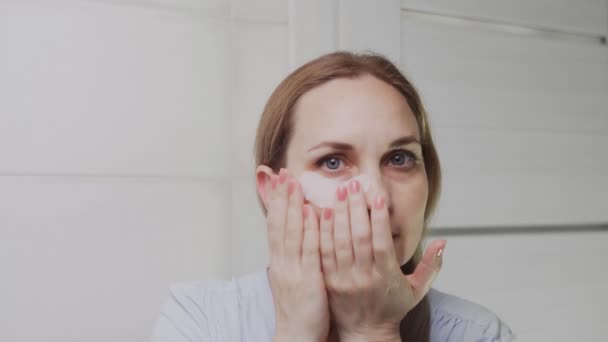 Zbliżenie dorosłej kobiety wkłada klocki kolagenowe pod oczy i patrzy w kamerę — Wideo stockowe