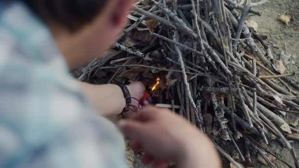 Sobre la vista del hombro del viajero hombre utiliza un encendedor para hacer una hoguera en el prado en el bosque de otoño — Vídeo de stock