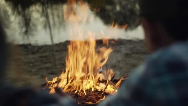 Visão traseira de homem e mulher viajantes senta-se perto da fogueira e fritas marshmallows nas varas — Vídeo de Stock