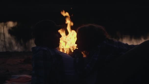 Siluet pasangan muda yang berbaring di dekat api unggun saling memandang satu sama lain dan berciuman, di luar ruangan — Stok Video